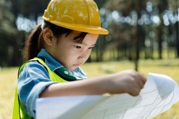 Happy child girl wearing yellow construction helmet or safety hard hat.