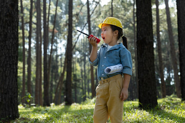 Little girl in safety helmet holding blueprints and talking on a walkie-talkie.