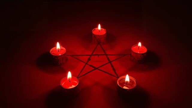 Starting shot showing five red tea-lights flickering on dark table in pentagram shape, wax dripping