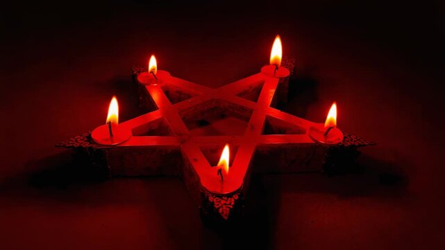 Camera recording flickering candle flames above pentagram candle holder on wooden surface