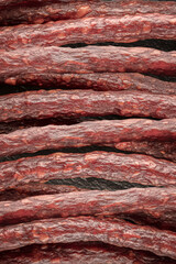 Delicious, thin smoked sausages are laid out in a close-up view, showcasing their rich red color and appealing texture. Perfect snack for gatherings or solo enjoyment.