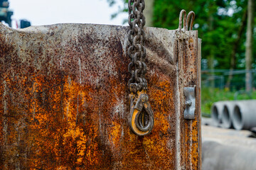 Heavy chain hook attached to a rusted crane rigging at a construction site during daytime