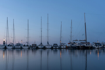 Fototapeta premium Calm evening at the marina with sailboats lined up reflecting in tranquil waters