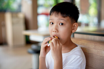 young boy is eating a sandwich, Asian boy is happily eating food