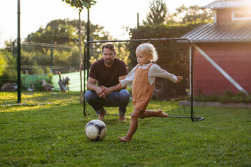 Little boy playing football with father in backyard.
