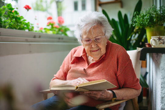 Senior lady sitting at balcony, reading book.
