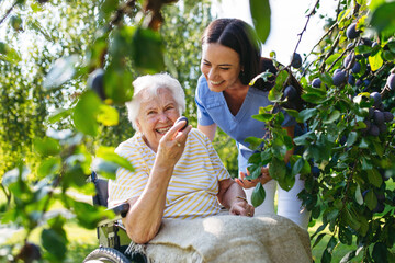 Home nurse spending time with elderly lady patient in garden.