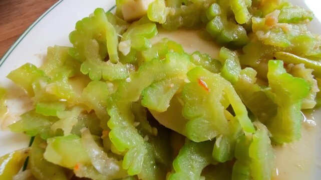 A close-up image of Indonesian-style stir-fried bitter melon (pare) cooked with garlic, chili, and tofu. This traditional Asian dish is known for its slightly bitter flavor and is often enjoyed