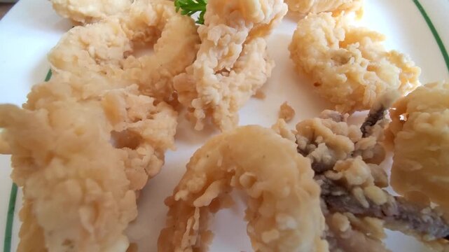 A close-up image of golden crispy fried calamari rings served on a white plate. This popular seafood appetizer is made from squid coated in seasoned flour and deep-fried until crunchy