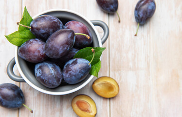 Fresh ripe plums in bowl on wooden table