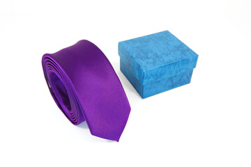 Purple tie rolled on white background with gift box together closeup view 