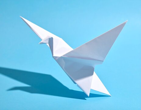 white origami dove with a striking shadow, soaring over a vibrant blue background. symbol of peace and hope.