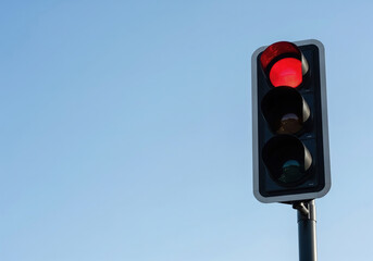 Red traffic light. A red light indicating to stop in front of a clear blue, cloudless sky. On the right, text copy area on the left.