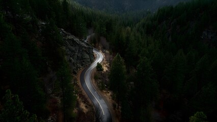 Winding mountain road curving through a dense pine forest beside rocky cliffs, seen from above. Concept Bird's-eye view, Winding mountain road, Dense pine forest, Rocky cliffs, Scenic landscape