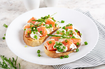Two open sandwich, toast with salmon, cream cheese, green onions for healthy breakfast on white plate.