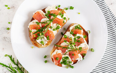 Two open sandwich, toast with salmon, cream cheese, green onions for healthy breakfast on white plate. Top view