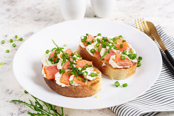 Two open sandwich, toast with salmon, cream cheese, green onions for healthy breakfast on white plate.