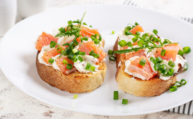 Two open sandwich, toast with salmon, cream cheese, green onions for healthy breakfast on white plate.