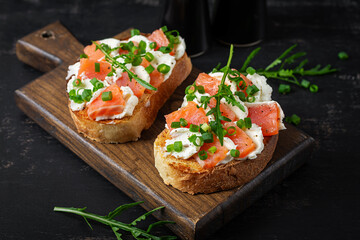 Salmon sandwiches, salted fish,  cream cheese and green onion on wooden background. Healthy breakfast with salmon toasts