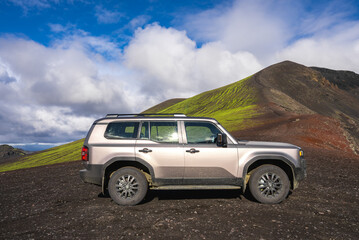 A silver 4x4 SUV rests on black lava gravel near Landmannalaugar, Iceland, daylight highlights...
