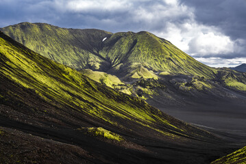 Ribbed green ridges sweep to a dark lava plain in Landmannalaugar, Iceland. Low late afternoon...
