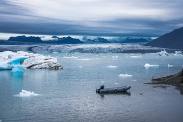 A small inflatable boat floats near shore on Jokulsarlon Glacier Lagoon, Iceland. Blue white...