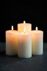 A minimalist candle arrangement, symbolizing light, hope, and enduring memory. A low angle shot focusing on a cluster of unscented white pillar candles of varying heights arranged on a smooth, dark