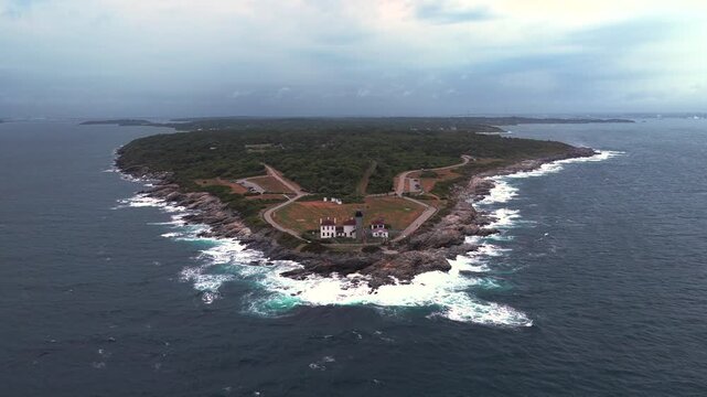 Aerial view of Conanicut Island and Beavertail Lighthouse in Beavertail State Park at the entrance to Narragansett Bay. The camera dolly in towards the tip of the island and lighthouse on a cloudy day