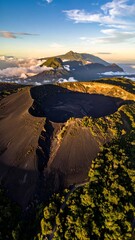Aerial view of a large volcanic crater and mountainous terrain under a partly cloudy blue sky during golden hour