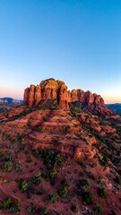 Aerial view of a striking red sandstone formation under a vibrant, clear blue sky during dusk, casting golden hues