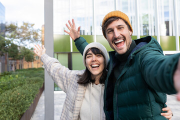 Happy couple taking selfie while visiting modern city during winter vacation