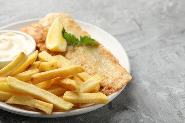 British Traditional Fish and chips with sauce, lemon and parsley on gray textured table, closeup