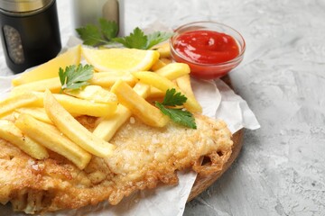 British Traditional Fish and chips with sauce, lemon and spices on gray textured table, closeup