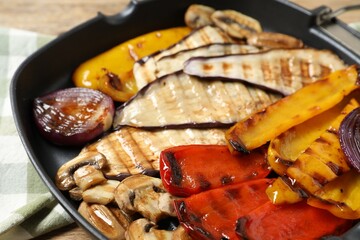 Tasty grilled vegetables and mushrooms in pan on wooden table, closeup