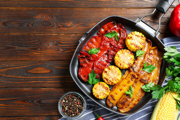 Delicious grilled vegetables in pan and spices on wooden table, flat lay. Space for text