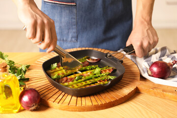Man adding onion into pan with grilled vegetables at table indoors, closeup