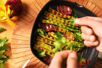 Man adding parsley into pan with grilled vegetables at table, top view
