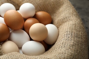 Many raw chicken eggs in sack on grey table, closeup