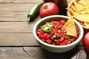 Tasty salsa with nachos and ingredients on wooden table, closeup