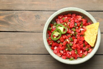 Tasty salsa with nacho chip on wooden table, top view. Space for text