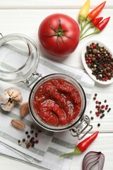 Tasty salsa sauce in jar and ingredients on white wooden table, flat lay
