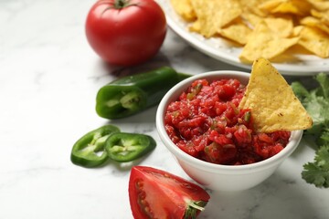 Tasty salsa in bowl, ingredients and nachos on white marble table, closeup. Space for text