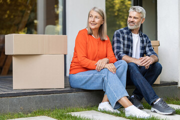 Happy senior couple sitting outside home near moving boxes