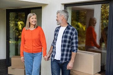 Senior couple holding hands together smiling with moving boxes in background