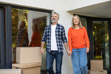 Senior couple enjoying moving day holding hands near doorway and boxes