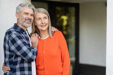 Senior man and woman smiling while standing on porch of their new house