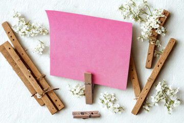 Pink paper note held by clothespins surrounded by flowers and wood