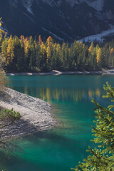 Breathtaking view of Lake Braies, Dolomites, Italy - crystal-clear turquoise water, surrounded by autumn-colored trees and dramatic mountain scenery.