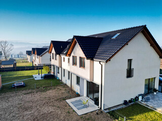 Nowoczesny dom na osiedlu z widokiem na błękitne niebo. Jasna elewacja, duże okna i prosta forma podkreślają współczesny styl architektury. Ujęcie oddaje harmonię między nowoczesnym budownictwem a spo © Freshfanpage