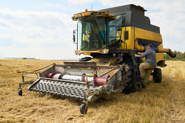 Fototapeta premium Middle aged Caucasian man climbing onto large combine harvester in wheat field during harvest season, operating agricultural machinery, rural landscape visible in background